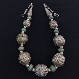 May include: A silver necklace with large, ornate, silver beads and turquoise spacers. The necklace has a silver chain with a cone-shaped pendant at each end.