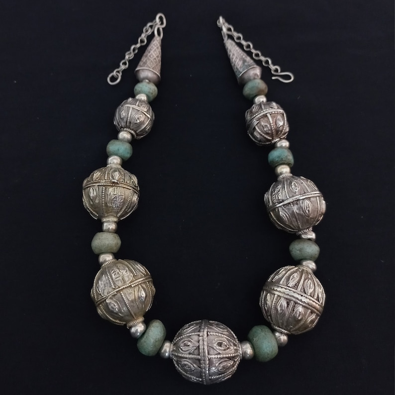 May include: A silver necklace with large, ornate, silver beads and turquoise spacers. The necklace has a silver chain with a cone-shaped pendant at each end.