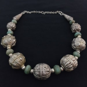 May include: A silver necklace with large, round, ornate beads and smaller, green beads. The beads are connected by a silver chain.