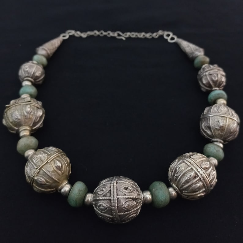 May include: A silver necklace with large, round, ornate beads and smaller, green beads. The beads are connected by a silver chain.