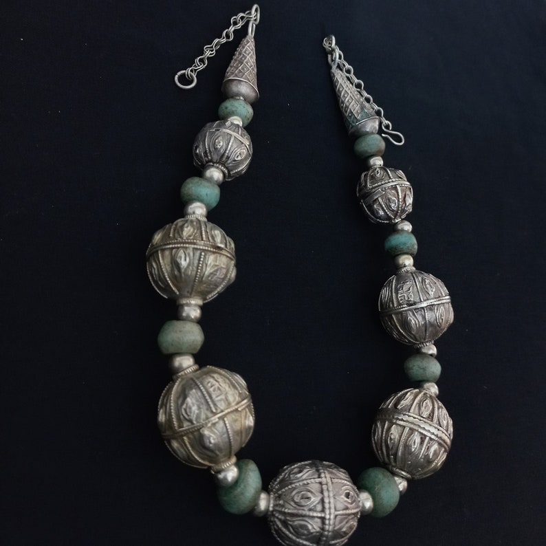 May include: A silver and turquoise beaded necklace with large, ornate silver balls. The necklace has a silver chain closure.