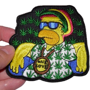 May include: An embroidered patch featuring a cartoon character wearing a yellow shirt, sunglasses, and a red, yellow, and green hat. The character is sitting in a chair with a green leaf pattern. The patch has a black background with green leaf patterns and a yellow circle with the text "One Love" in the center.