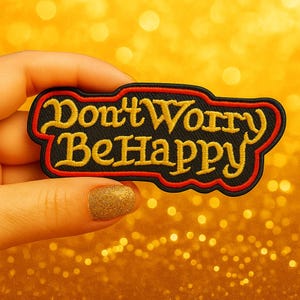 Peut inclure: Un écusson brodé noir avec l'inscription "Don't Worry Be Happy" en lettres jaunes. Le patch a une bordure rouge et est présenté sur un fond doré scintillant.