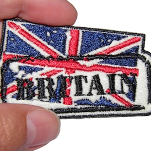 Peut inclure: Un écusson brodé blanc avec un drapeau britannique rouge, blanc et bleu et le mot "BRITAIN" en lettres noires.