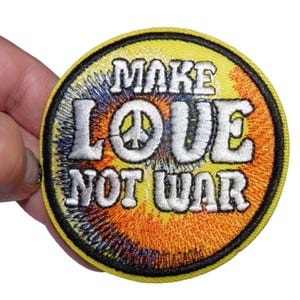 May include: A yellow, round embroidered patch with a peace sign and the text "Make Love Not War" in white.