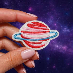 Può includere: Toppa ricamata con un design a forma di pianeta. Il pianeta ha strisce rosse e rosa con un anello blu. La toppa è bianca con un bordo cucito. Lo sfondo è una galassia viola.