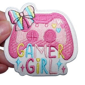 Può includere: Toppa ricamata rosa e bianca con un controller per videogiochi rosa, un fiocco arcobaleno e il testo "Gamer Girl" con accenti glitter.