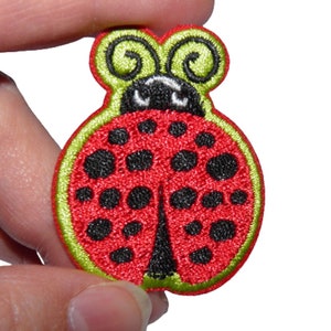 Peut inclure: Patch brodé représentant une coccinelle rouge et noire avec des antennes vertes.