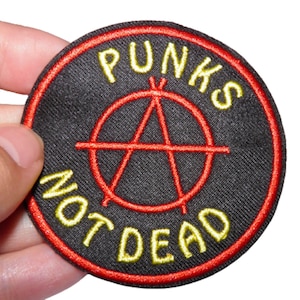 Peut inclure: Un écusson brodé noir et rouge avec le texte "Punks Not Dead" et un symbole d'anarchie au centre.