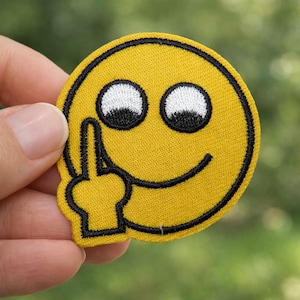 Peut inclure: Écusson brodé jaune représentant un smiley avec un majeur levé. Le patch a des contours noirs, des yeux blancs et un sourire noir. Le patch est rond et a un fond jaune.