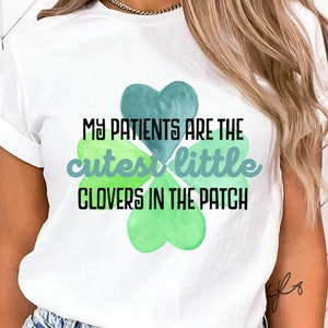 May include: White t-shirt with a green four-leaf clover design and the text "My patients are the cutest little clovers in the patch."