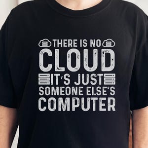 Könnte beinhalten: Schwarzes T-Shirt mit dem weißen Text "THERE IS NO CLOUD IT'S JUST SOMEONE ELSE'S COMPUTER". Das Shirt hat einen Rundhalsausschnitt und kurze Ärmel. Die Person, die das Shirt trägt, lächelt.