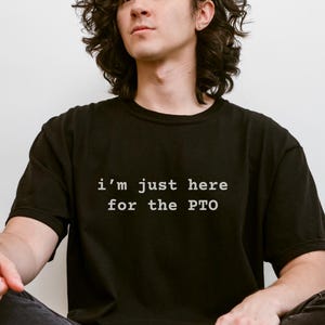 May include: A person wearing a black t-shirt with the text "i'm just here for the PTO" in white.
