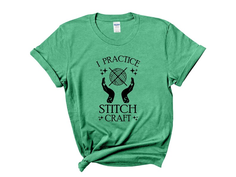 K&ouml;nnte beinhalten: Gr&uuml;nes T-Shirt mit dem Text "I practice stitch craft" in schwarzer Schrift. Der Text ist von Sternen und einer Grafik von H&auml;nden umgeben, die eine Wollkn&auml;uel halten.