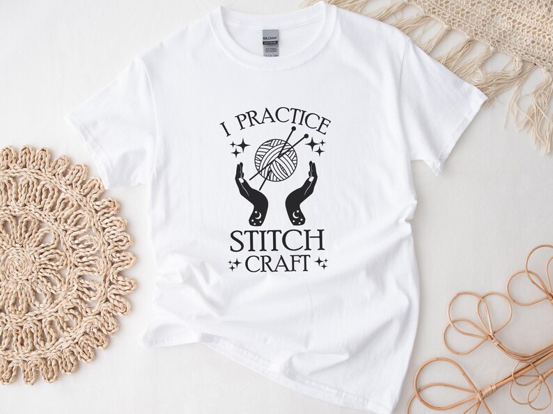 May include: White t-shirt with black text that reads "I practice stitch craft" with a graphic of two hands holding a ball of yarn and knitting needles.