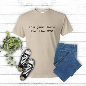 May include: A beige t-shirt with the text "i'm just here for the PTO" printed in black.