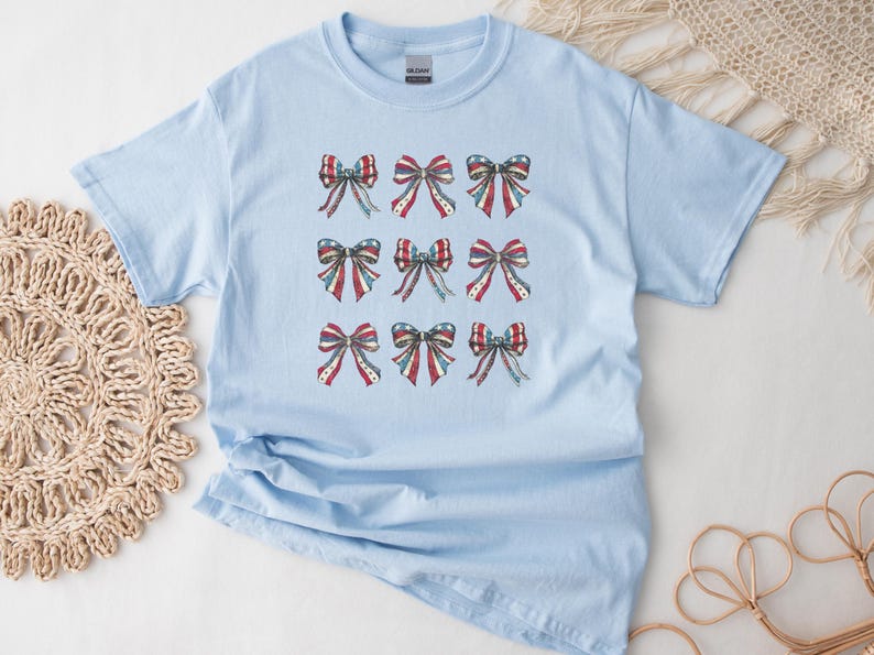 Puede incluir: Camiseta azul claro con nueve dise&ntilde;os de lazos en rojo, blanco y azul, que recuerdan a la bandera estadounidense. Los lazos tienen un efecto acuarela, a&ntilde;adiendo un toque suave al tema patri&oacute;tico. La camiseta es de material suave.