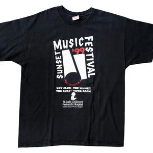 May include: Black t-shirt featuring the text "Sunset Music Festival '99" in white and red. The shirt also lists the Key Club, The Whisky, The Roxy, and Viper Room. The shirt is a vintage concert tee.
