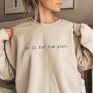 May include: A sand-colored sweatshirt with the text "do it for the plot." printed on the front.