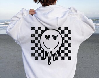 May include: White hoodie with a black and white checkered design and a melting smiley face with heart eyes. The text "WHITE HOODIE" is at the bottom of the image. The hoodie is made of a soft material.