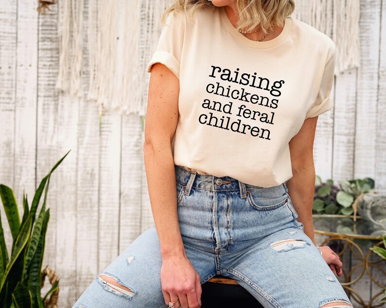 Cream-colored short-sleeve t-shirt featuring the black text raising chickens and feral children printed on the front