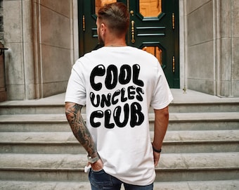 May include: A white short-sleeved t-shirt featuring the black text COOL UNCLES CLUB printed in a bold, rounded, bubble-style font on the back. The shirt is worn with dark blue denim jeans, showcasing a casual and simple design aesthetic.