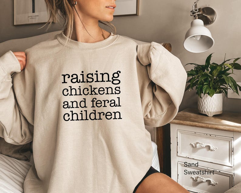 Sand-colored crewneck sweatshirt featuring the black text raising chickens and feral children printed on the front