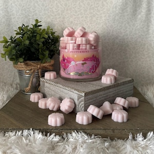 May include: A pink glass jar candle with a white label that reads "Swirled Peppermint" surrounded by pink wax melts in the shape of flowers.