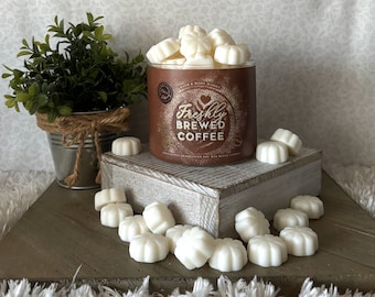 May include: A brown glass jar filled with white wax melts. The jar has a gold label with the text "Freshly Brewed Coffee" and a heart design. The wax melts are scattered around the jar on a wooden surface.