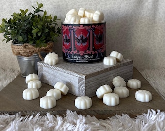 Può includere: Un barattolo cilindrico per candele con etichetta Vampire Blood riempito di cera profumata bianca a forma di piccole zucche. L'etichetta presenta un design gotico rosso e nero con pipistrelli. Altre cere bianche a forma di zucca sono sparse.