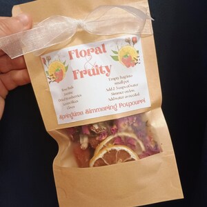 May include: A brown paper bag with a white ribbon tied around it. The bag contains a mix of dried fruit and flowers. The bag has a label that says "Floral & Fruity Springtime Simmering Potpourri". The label also includes instructions for using the potpourri.