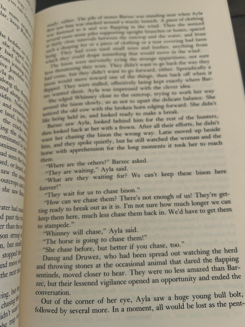 May include: Open book with printed text. The pages are yellowed, and the text is in black. The text is about a group of people chasing bison. The book is open to a specific page.
