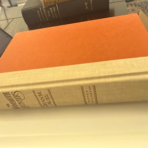 May include: A hardcover book titled "The Mammoth Hunters" by Jean M. Auel. The book has an orange cover and a cream-colored spine with the author's name and the publisher's name, "Crown."