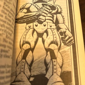 May include: Black and white illustration of a standing armored figure holding a sword. The figure is wearing a helmet and has detailed armor plating. The image is from a book and is surrounded by text.