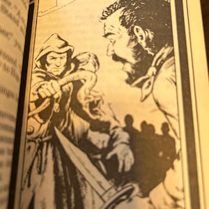 May include: Black and white illustration from a book depicting a hooded figure holding a dagger, facing a man with a beard. The scene suggests a confrontation, with other figures in the background. The artwork is framed by a decorative border.