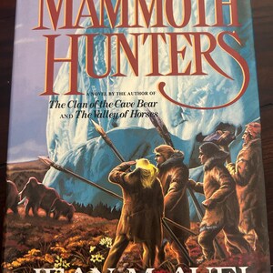 May include: A book cover for "The Mammoth Hunters" by Jean M. Auel. The title is in large, orange letters against a blue background. The cover art depicts figures with spears, mammoths, and the text "Earth's Children".