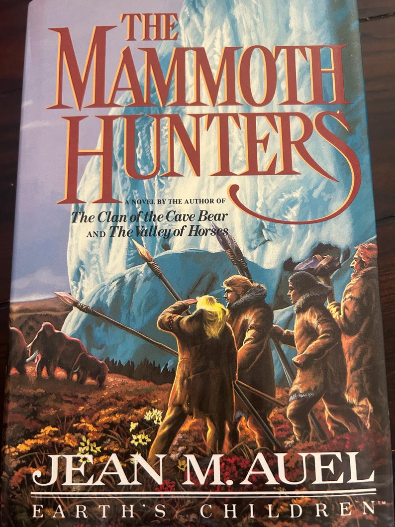 May include: A book cover for "The Mammoth Hunters" by Jean M. Auel. The title is in large, orange letters against a blue background. The cover art depicts figures with spears, mammoths, and the text "Earth's Children".