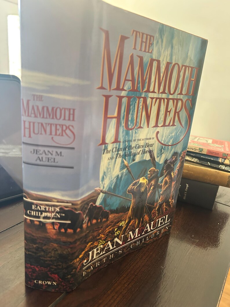 May include: A hardcover book titled "The Mammoth Hunters" by Jean M. Auel. The cover features a landscape with mammoths and figures, with the title in large, stylized letters. The book is part of the "Earth's Children" series.