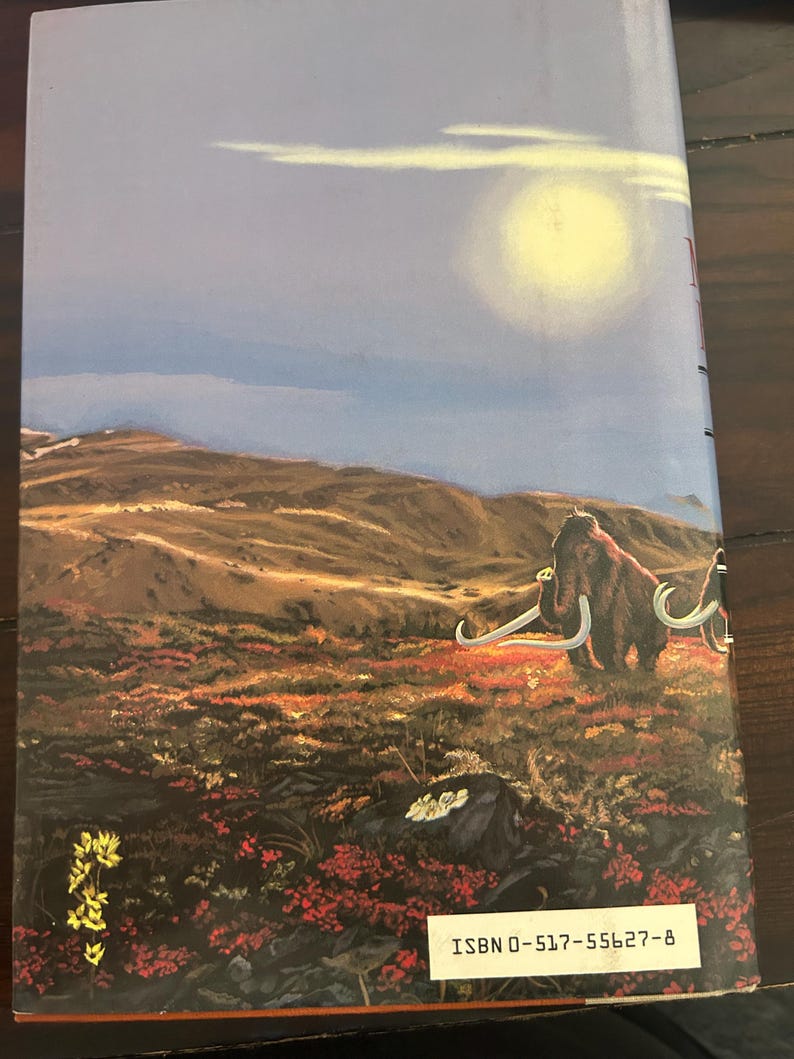 May include: Book cover featuring a landscape with a woolly mammoth. The background shows a sky with a bright sun and rolling hills. The foreground is filled with red and green vegetation. The book's ISBN is visible.