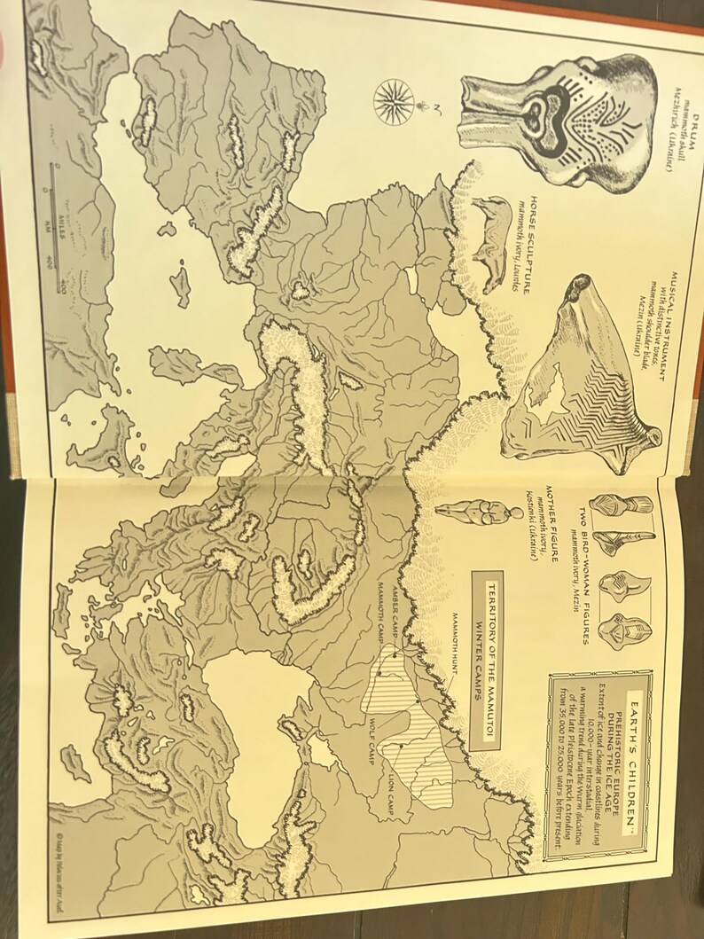 May include: An open book displays a map of prehistoric Europe during the Ice Age, with illustrations of artifacts and text. The map shows the territory of the Mamutoi winter camps and includes illustrations of a drum, horse sculpture, and mother figure.