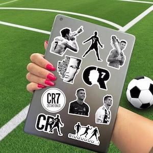 Puede incluir: Un conjunto de pegatinas en blanco y negro con Cristiano Ronaldo en varias poses y el logotipo CR7. Las pegatinas est&aacute;n en una tableta, con un bal&oacute;n de f&uacute;tbol en el fondo. Tambi&eacute;n se ve el texto "Your love makes me strong, your hate makes me unstoppable".