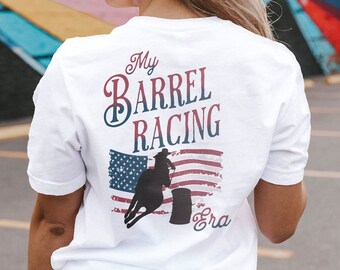 May include: White t-shirt with a graphic of a barrel racer and the text "My Barrel Racing Era" on the back. The graphic features a distressed American flag.