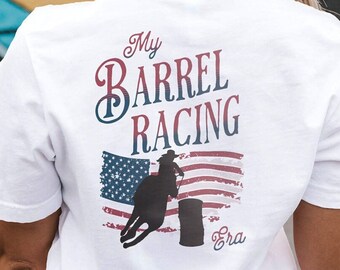 May include: A white short-sleeved t-shirt featuring a graphic on the back with the text My BARREL RACING Era. The design includes a silhouette of a person riding a horse around a barrel, set against a distressed American flag background.