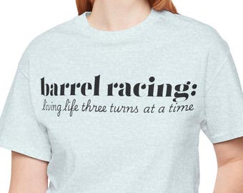 May include: A light blue t-shirt with the text "barrel racing: living life three turns at a time" in black.