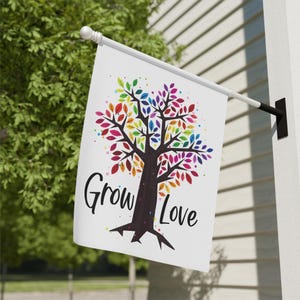 May include: A white garden flag featuring a rainbow tree and the text "Grow Love".