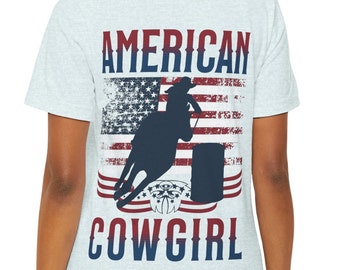 May include: Pale grey t-shirt with a distressed American flag design and a silhouette of a cowgirl riding a horse around a barrel. The words "AMERICAN COWGIRL" are printed in navy blue and red.