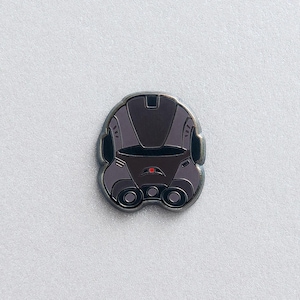 Op de afbeelding: Een zilveren en grijze emaille pin van een robotkop met een rood oog. De robot heeft een donkergrijs vizier en een donkergrijs lichaam.