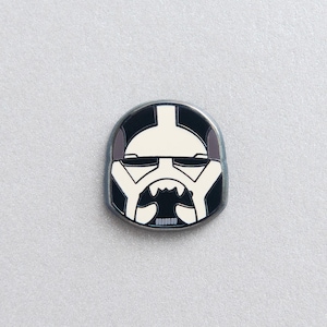 May include: A black and white enamel pin featuring a stylised depiction of a Star Wars Stormtrooper helmet.
