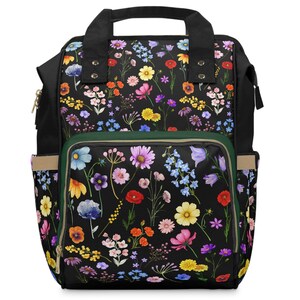 Könnte beinhalten: Schwarzer Rucksack mit einem Blumenmuster mit verschiedenen bunten Blumen auf schwarzem Hintergrund. Der Rucksack hat eine grüne Reißverschlusstasche und verstellbare Träger.