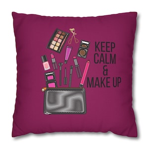 Può includere: Un cuscino color granata con una grafica in bianco e nero di una trousse da trucco con vari articoli da trucco che ne fuoriescono. Il testo "KEEP CALM & MAKE UP" è stampato sul cuscino.